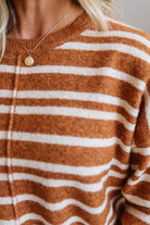 Close-up of a person wearing a fuzzy knit sweater with horizontal rust-brown and off-white stripes, along with a delicate gold necklace.