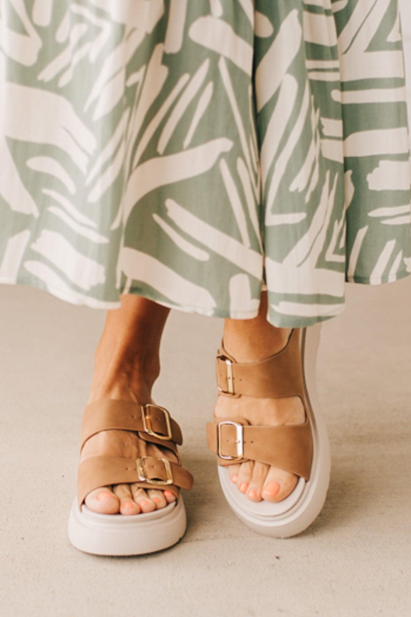Woman wearing double buckle platform slide sandals with cream sole and cognac vegan leather upper.
