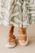 Woman wearing double buckle platform slide sandals with cream sole and cognac vegan leather upper.