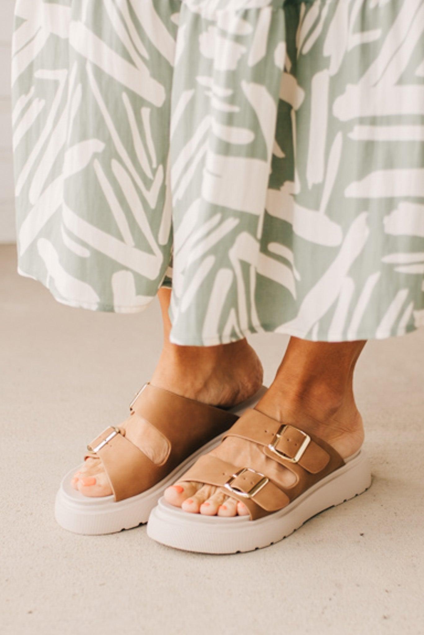 Woman wearing double buckle platform slide sandals with cream sole and cognac vegan leather upper.