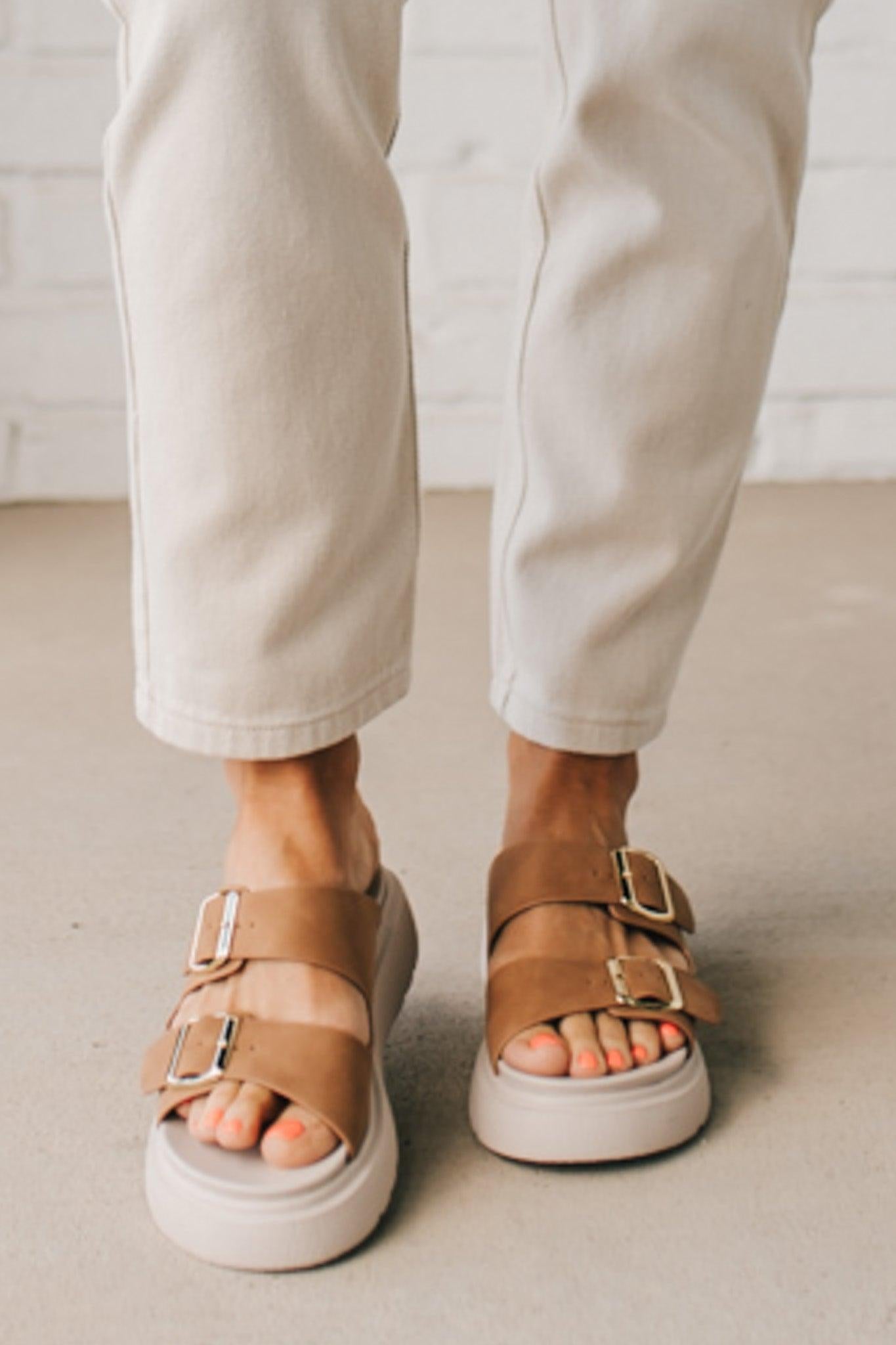 Woman wearing double buckle platform slide sandals with cream sole and cognac vegan leather upper.
