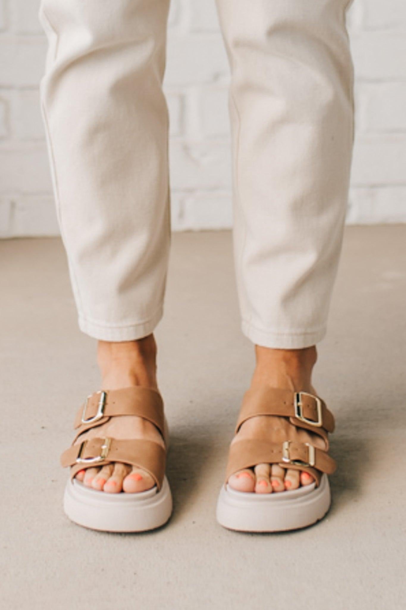 Woman wearing double buckle platform slide sandals with cream sole and cognac vegan leather upper.