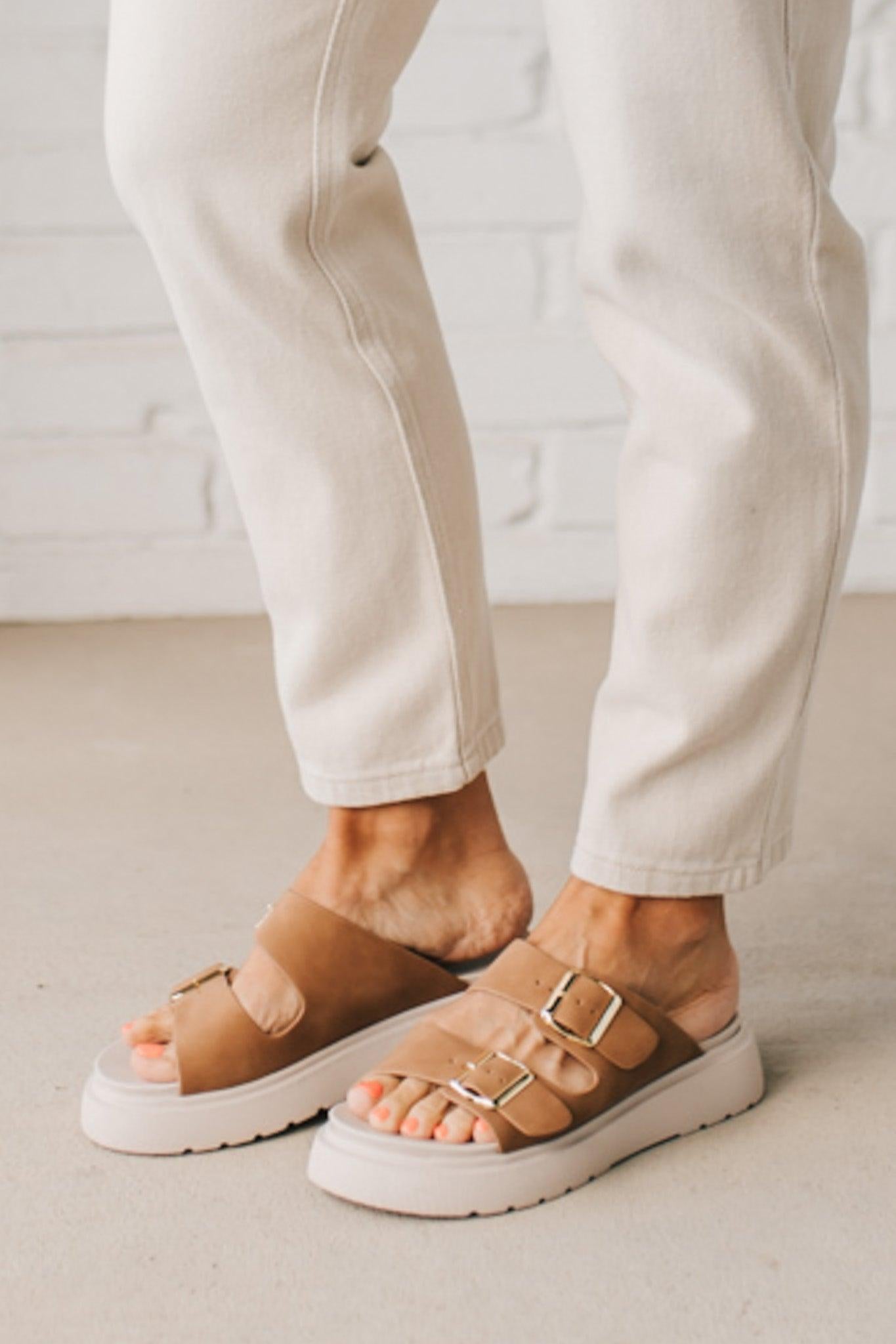 Woman wearing double buckle platform slide sandals with cream sole and cognac vegan leather upper.