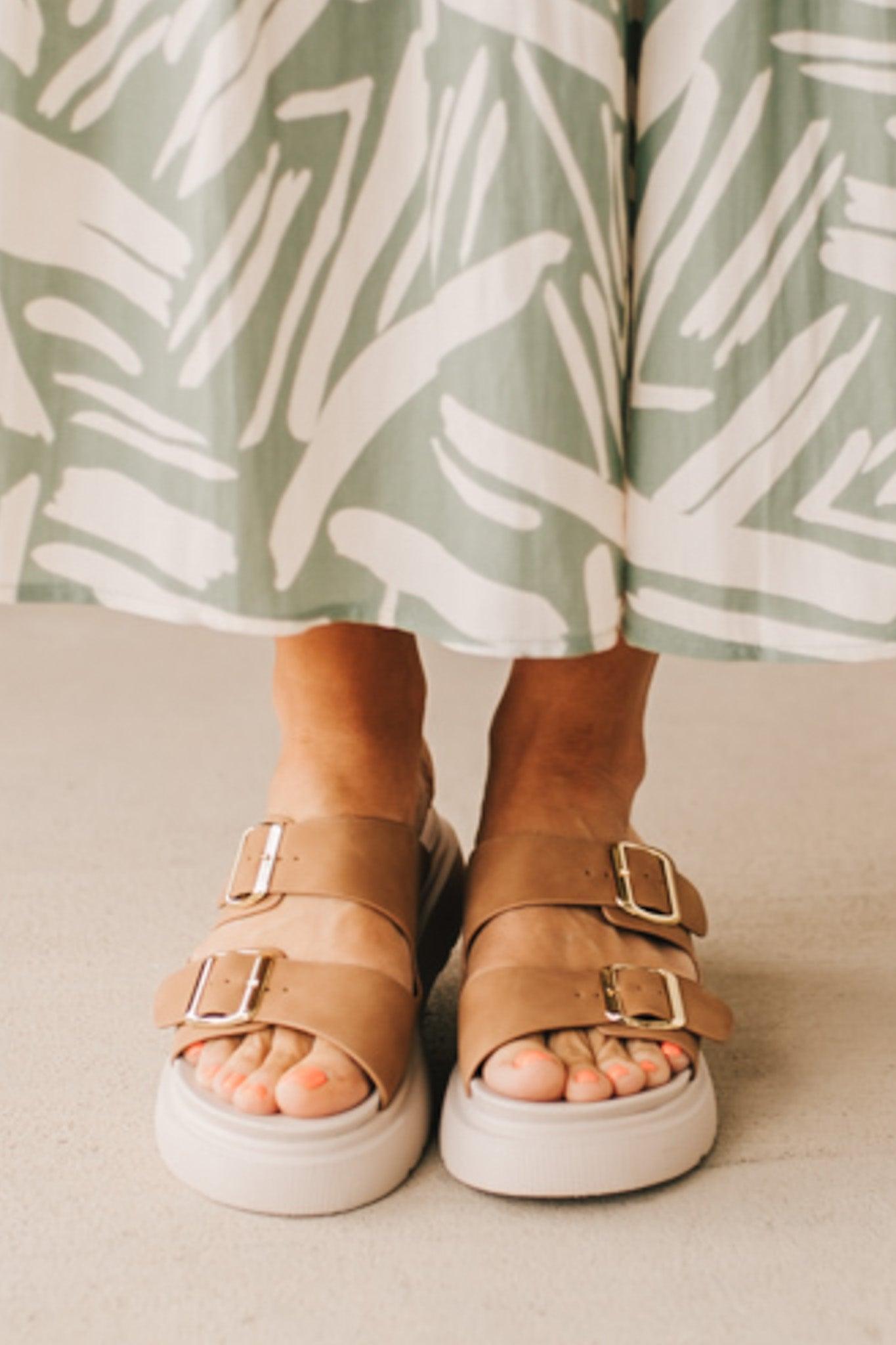 Woman wearing double buckle platform slide sandals with cream sole and cognac vegan leather upper.