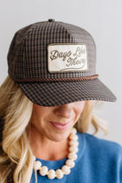 Blonde smiling woman wearing a plaid hat with a brown rope across the front, and a patch that is cream with brown embroidery that says Days Like These.