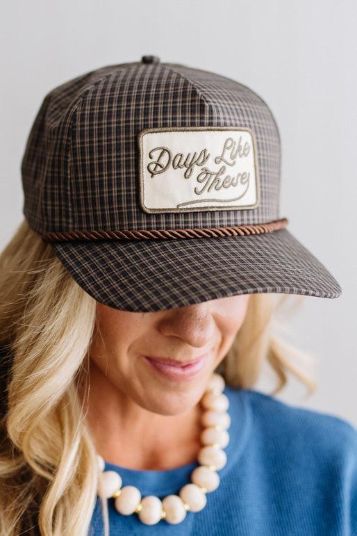 Blonde smiling woman wearing a plaid hat with a brown rope across the front, and a patch that is cream with brown embroidery that says Days Like These.