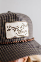 Blonde smiling woman wearing a plaid hat with a brown rope across the front, and a patch that is cream with brown embroidery that says Days Like These.