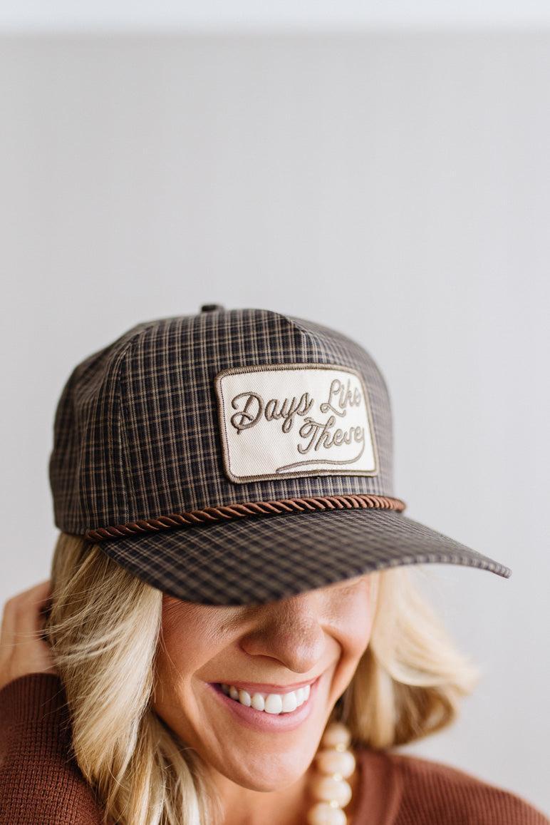 Blonde smiling woman wearing a plaid hat with a brown rope across the front, and a patch that is cream with brown embroidery that says Days Like These.