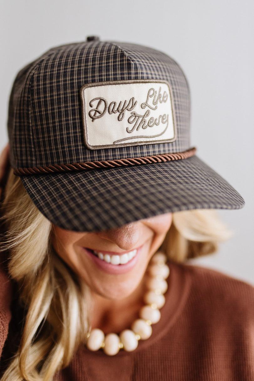 Blonde smiling woman wearing a plaid hat with a brown rope across the front, and a patch that is cream with brown embroidery that says Days Like These.