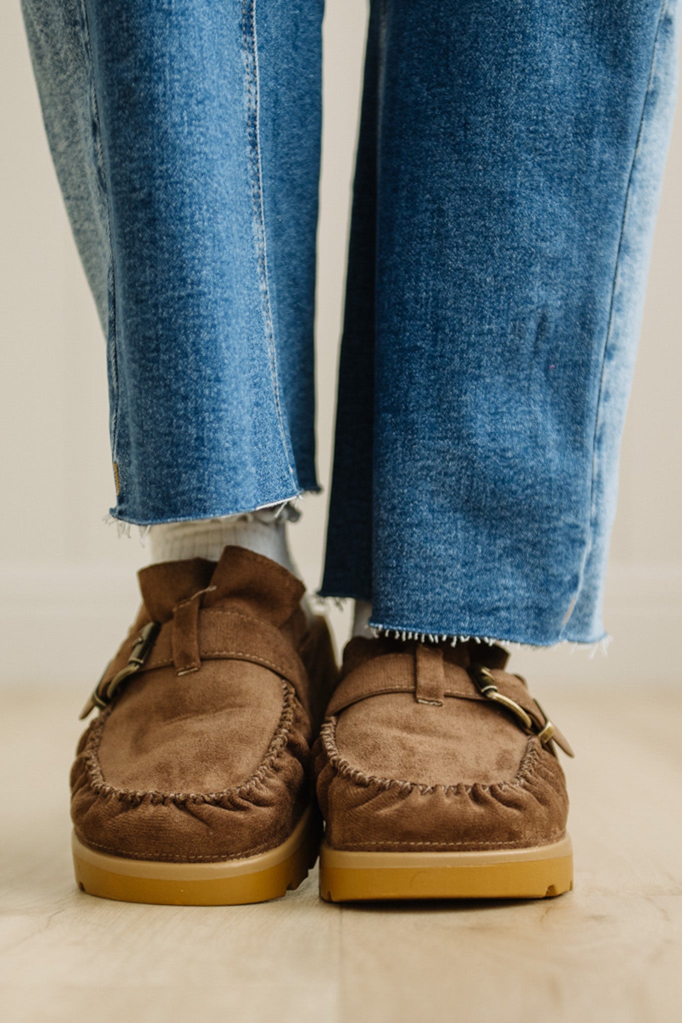 Brown moccasin shoes worn with blue jeans on a neutral background