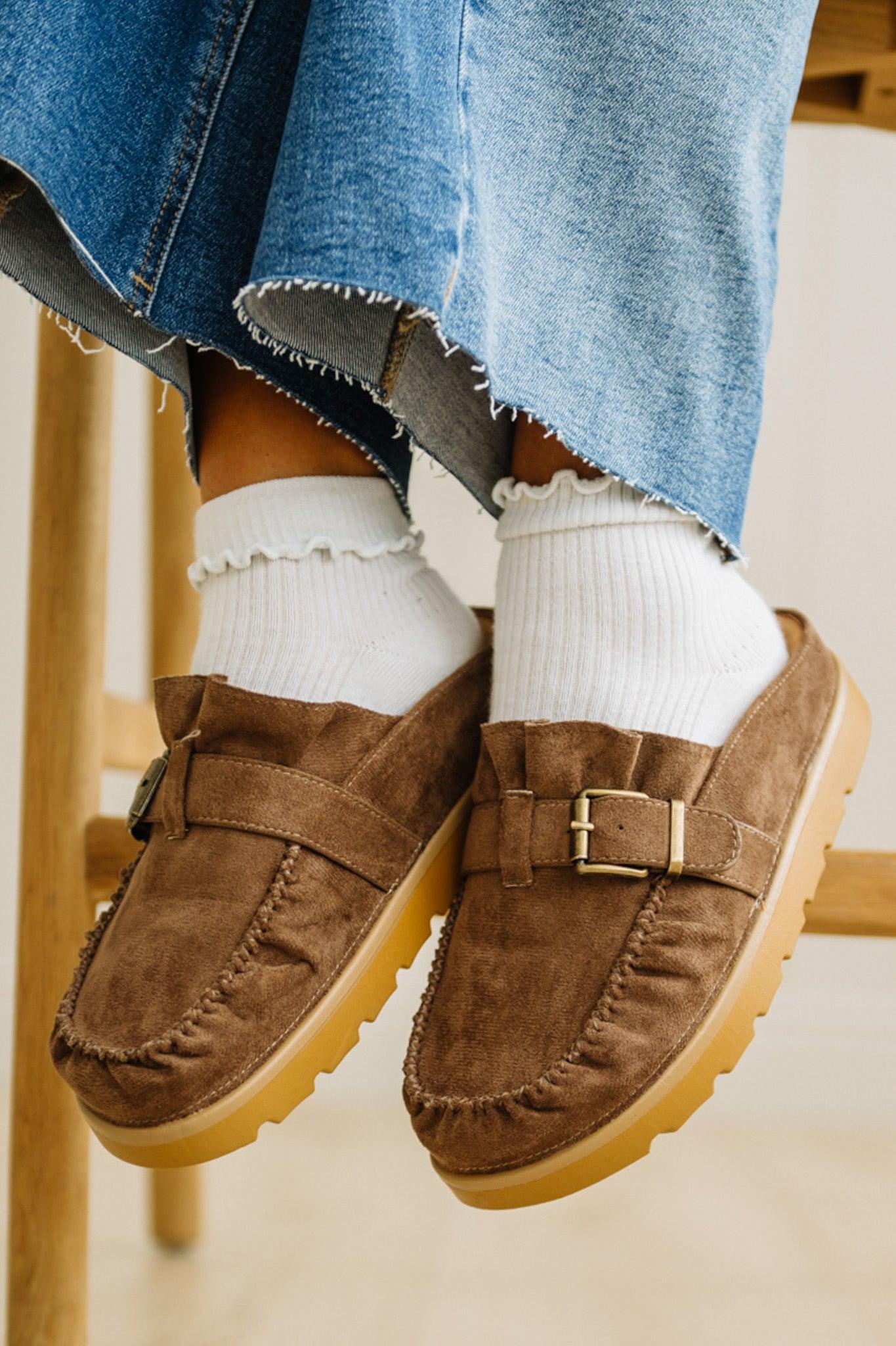 Brown suede loafers worn with white socks and blue jeans.