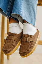 Brown suede loafers worn with white socks and blue jeans.
