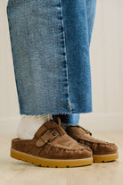 Brown suede shoes with buckles worn with blue jeans on a neutral background