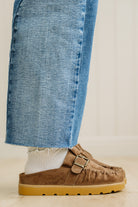 Brown suede shoes with tan soles worn with blue jeans on a neutral background
