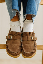 Brown suede loafers worn with white socks and blue jeans on a light background