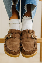 Brown moccasin shoes worn with white socks and blue jeans on a light background