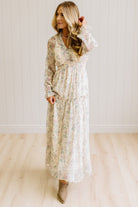 Woman wearing a cream floral dress against a white paneled wall.