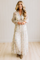 Woman wearing a cream floral dress against a white paneled wall.