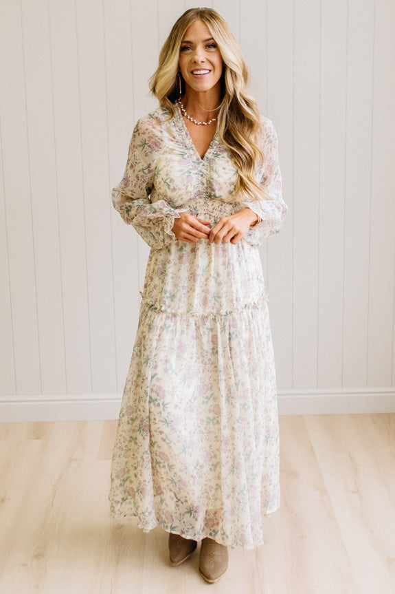 Woman wearing a cream floral dress against a white paneled wall.