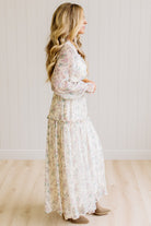 Woman wearing a cream floral dress against a white paneled wall.