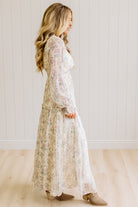 Woman wearing a cream floral dress against a white paneled wall.
