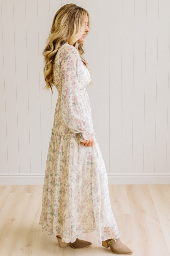 Woman wearing a cream floral dress against a white paneled wall.