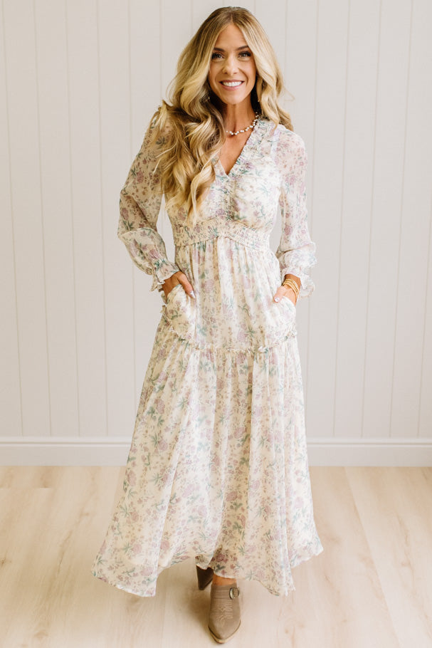 Woman wearing a cream floral dress against a white paneled wall.