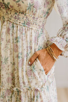 Woman wearing a cream floral dress against a white paneled wall.