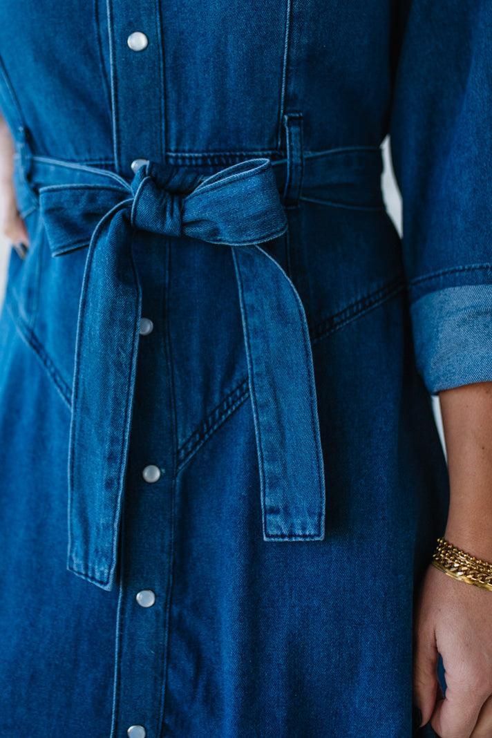 Blue denim dress with a belt and button details on a blurred background