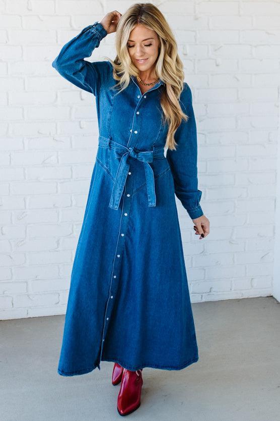 Woman wearing a blue denim dress with a white brick wall background