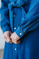 Close-up of a person wearing a blue denim jacket with white buttons.