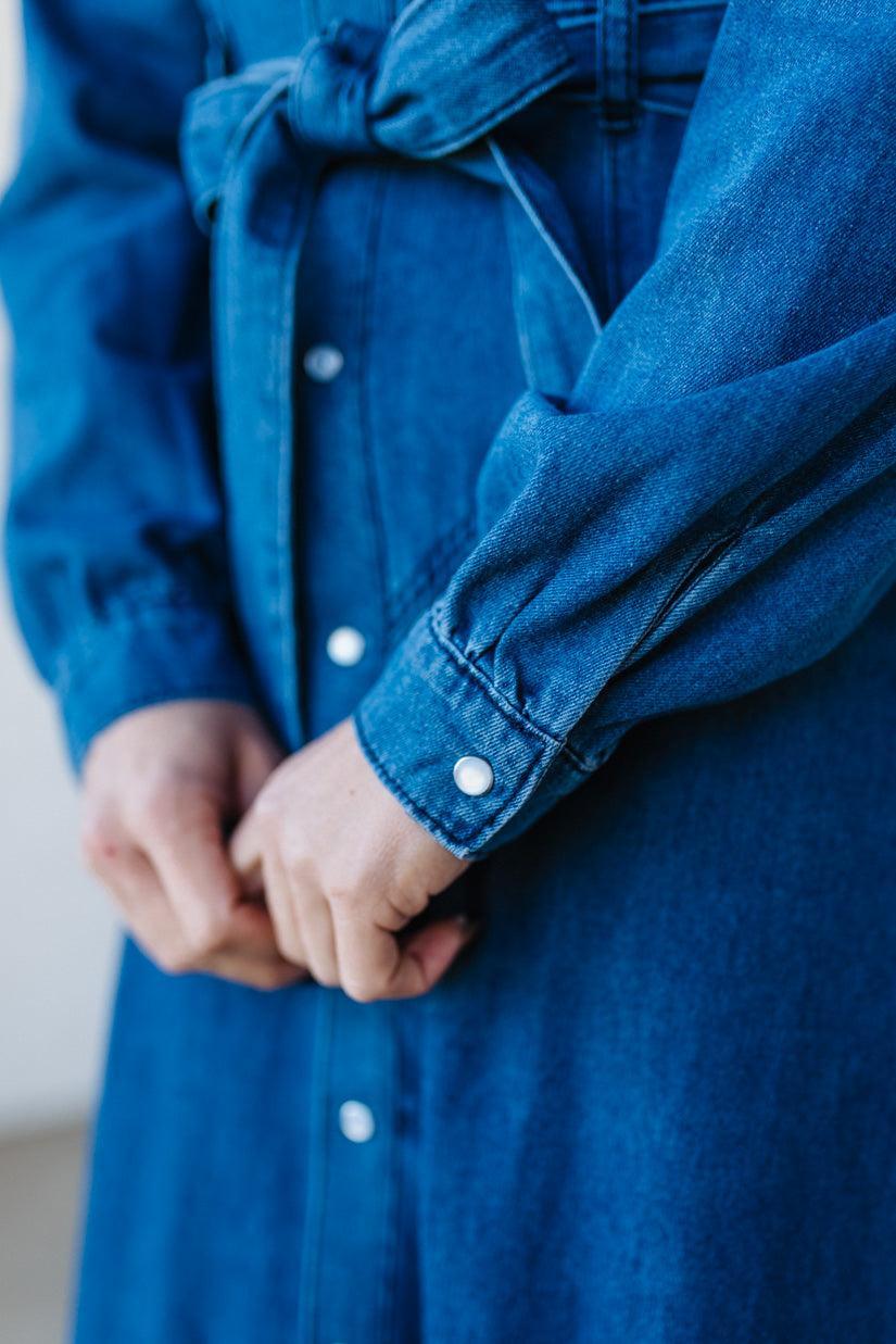 Close-up of a person wearing a blue denim jacket with white buttons.