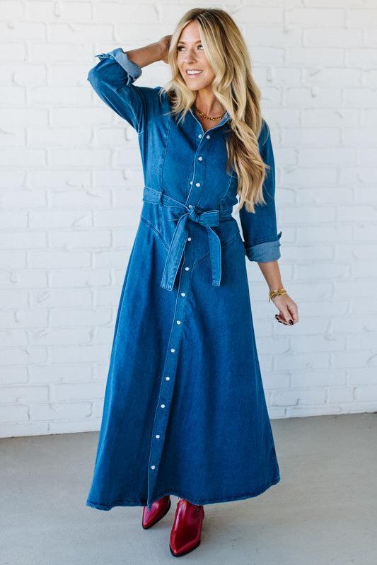 Woman wearing a blue denim dress with a white brick wall background