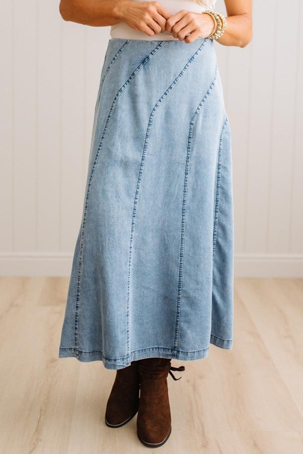 Blonde woman in a studio with light floor and a paneled wall behind, wearing a Denim Diagonal Line Detail Midi Skirt.