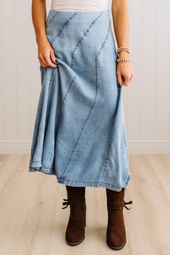Blonde woman in a studio with light floor and a paneled wall behind, wearing a Denim Diagonal Line Detail Midi Skirt.