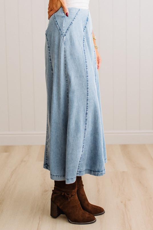 Blonde woman in a studio with light floor and a paneled wall behind, wearing a Denim Diagonal Line Detail Midi Skirt.