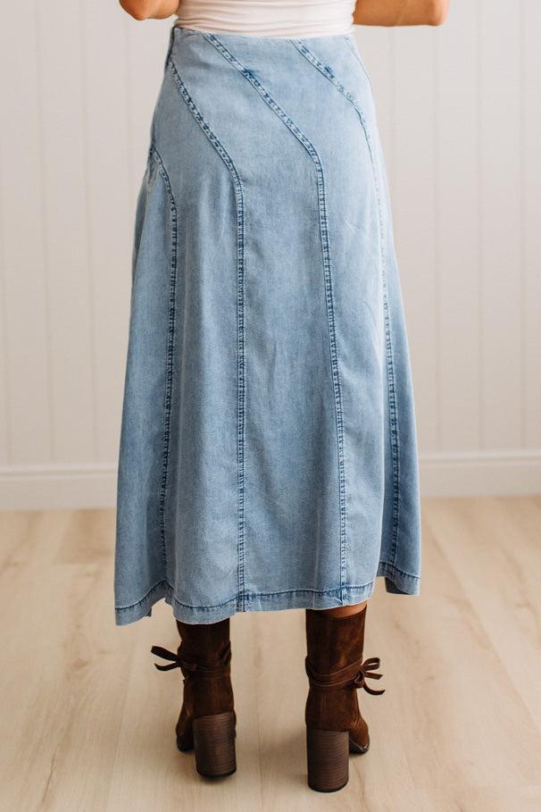 Blonde woman in a studio with light floor and a paneled wall behind, wearing a Denim Diagonal Line Detail Midi Skirt.
