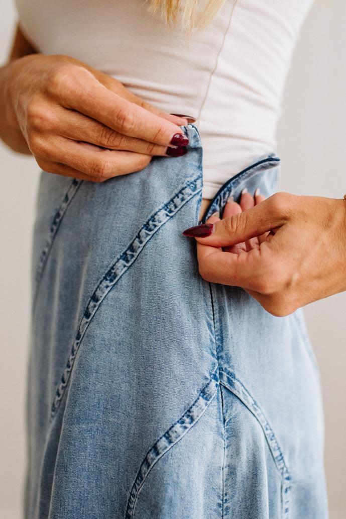 Blonde woman in a studio with light floor and a paneled wall behind, wearing a Denim Diagonal Line Detail Midi Skirt.