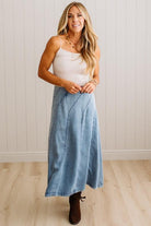 Blonde woman in a studio with light floor and a paneled wall behind, wearing a Denim Diagonal Line Detail Midi Skirt.