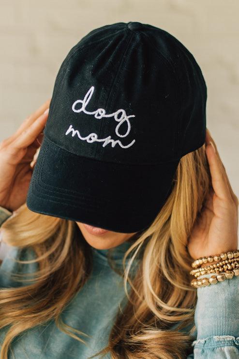Blonde woman wearing a black hat with white cursive embroidery that say "dog mom" at the center front.