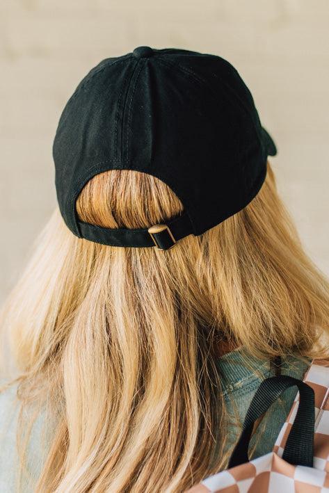 Blonde woman wearing a black hat with white cursive embroidery that say "dog mom" at the center front.