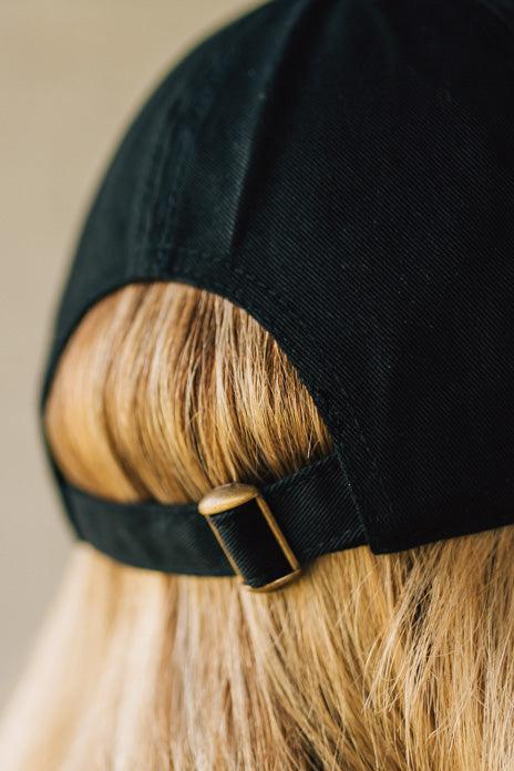 Blonde woman wearing a black hat with white cursive embroidery that say "dog mom" at the center front.