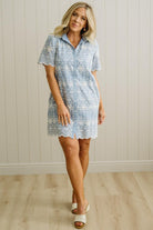 Blonde woman wearing a button front collared shift dress with scalloped edges, and all over eyelet lace embroidery in light blue chambray.