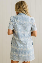 Blonde woman wearing a button front collared shift dress with scalloped edges, and all over eyelet lace embroidery in light blue chambray.