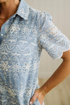 Blonde woman wearing a button front collared shift dress with scalloped edges, and all over eyelet lace embroidery in light blue chambray.