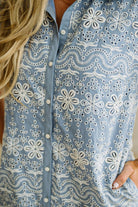 Blonde woman wearing a button front collared shift dress with scalloped edges, and all over eyelet lace embroidery in light blue chambray.