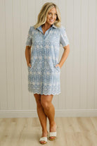 Blonde woman wearing a button front collared shift dress with scalloped edges, and all over eyelet lace embroidery in light blue chambray.