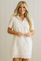 Blonde woman wearing a button front collared shift dress with scalloped edges, and all over eyelet lace embroidery in cream.