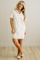 Blonde woman wearing a button front collared shift dress with scalloped edges, and all over eyelet lace embroidery in cream.