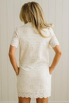 Blonde woman wearing a button front collared shift dress with scalloped edges, and all over eyelet lace embroidery in cream.